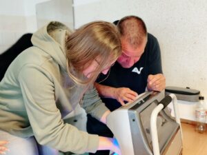 Schülerin hält Hände unter das UV-Gerät und Doktor Berger kontrolliert das Ergebnis