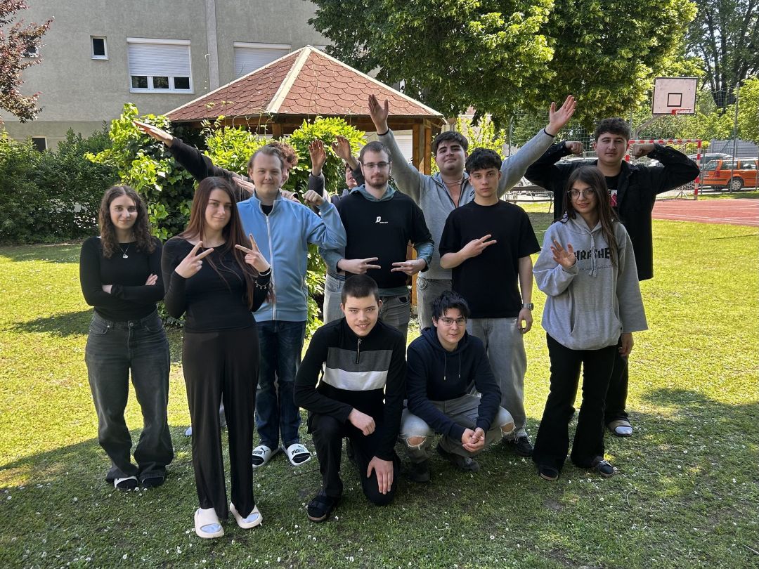 2025_26_Kommunikationsworkshop 1EH8_1 9 Schüler und 3 Schülerinnen im Schulgarten zeigen unterschiedliche Gesten mit den Händen