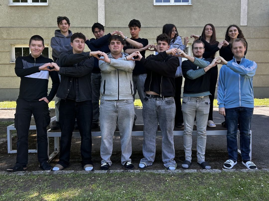 2025_26_Kommunikationsworkshop 1EH8_2 9 Schüler und 3 Schülerinnen im Schulgarten formen mit den Nachbarn jeweils ein Herzsymbol mit den Fingern