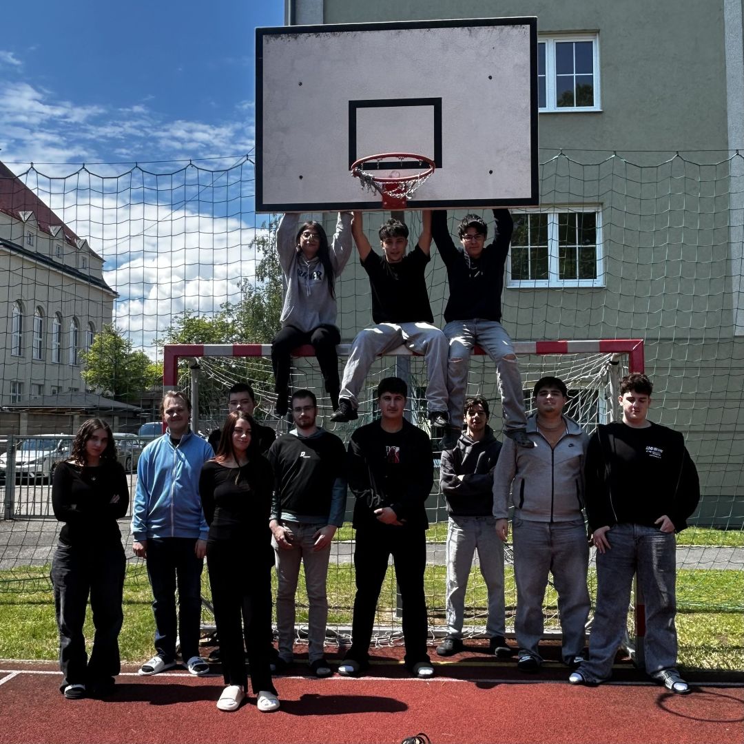 2025_26_Kommunikationsworkshop 1EH8_3 9 Schüler und 3 Schülerinnen im Schulgarten - 3 sitzen auf dem Fußballtor