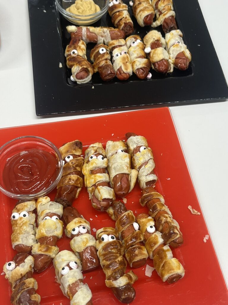 Zwei Platten mit Mumien, eingewickelte Würstel in Blätterteigstreifen, mit Ketchup und Senf als Dip in kleinen Schüsselchen